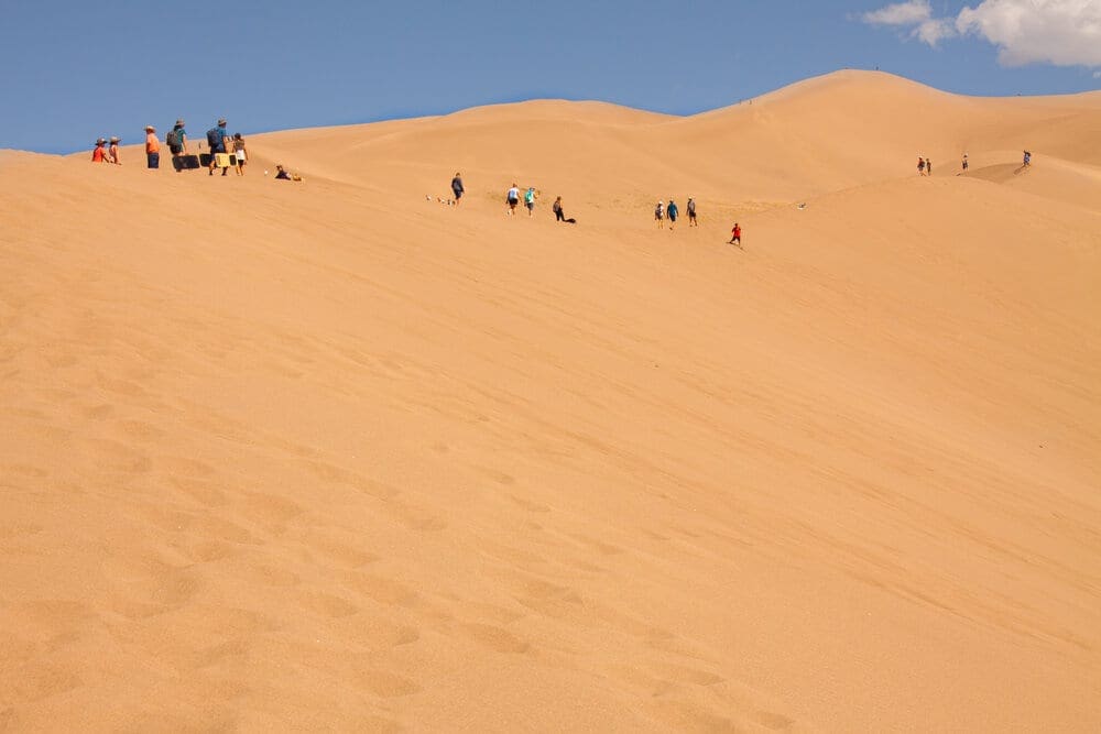Tourist hikers walk on giant desert sand dunes at the Great Sand Dunes National Park and Preserve.